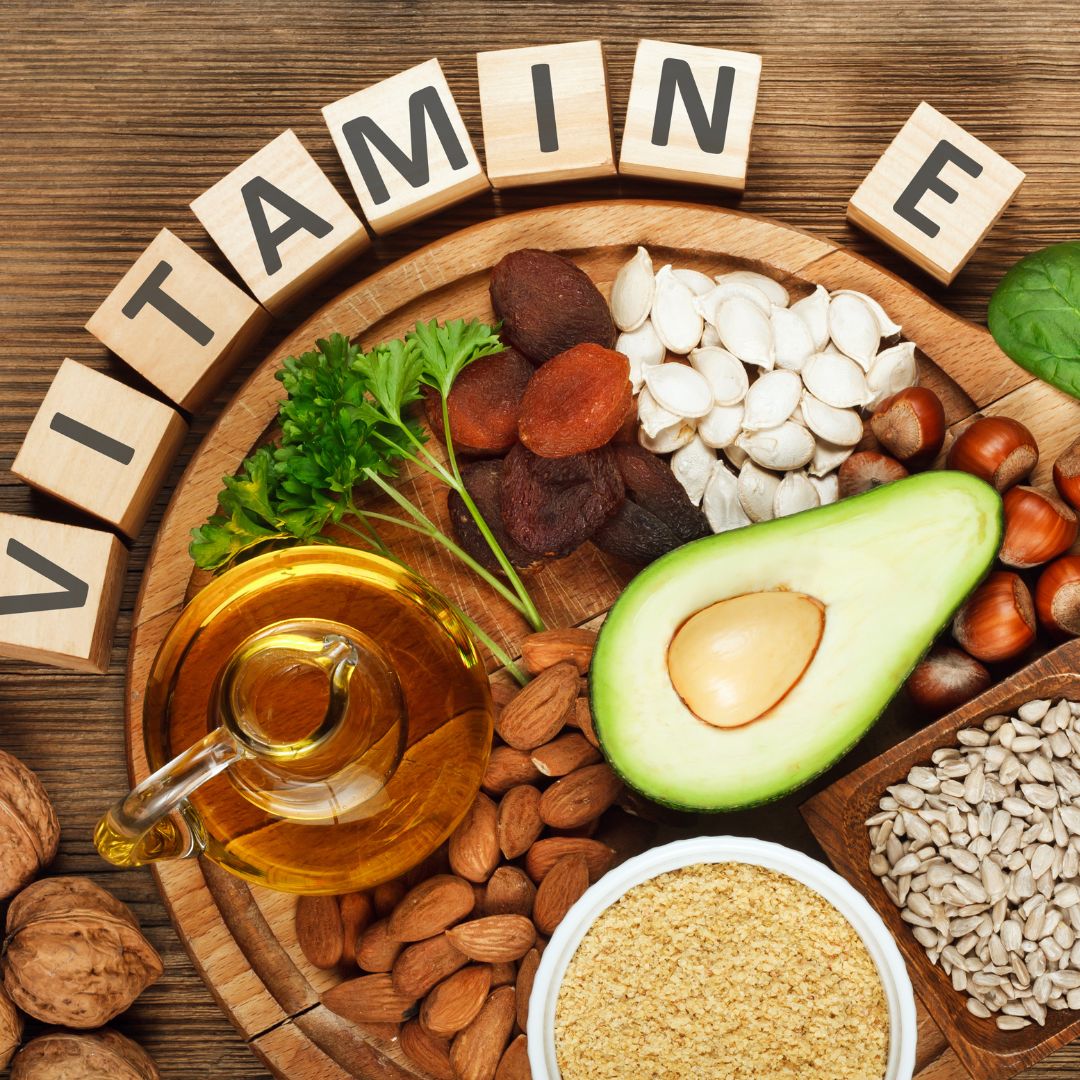 Aliments riches en vitamine E, y compris avocat, noix et graines, disposés en cercle avec des lettres formant le mot 'VITAMINE